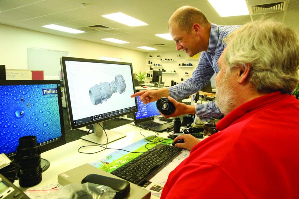 Engineer reviewing a 3D CAD model of a Philmac fitting on a computer screen while holding a physical component, illustrating product design, innovation, and environmental responsibility in fluid transfer solutions