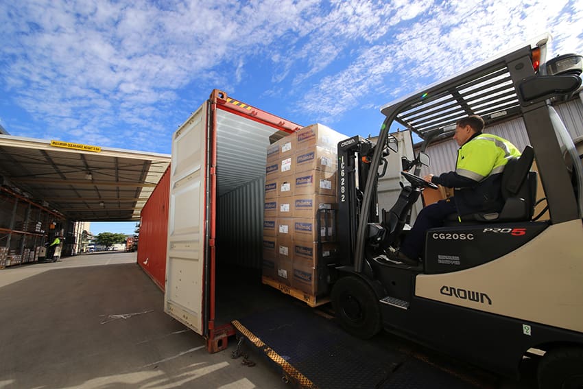Forklift loading a pallet of Philmac‑branded export cartons into a shipping container, illustrating global distribution and international product shipments.
